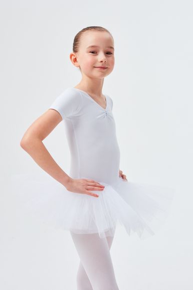 Ein junges Mädchen in einem weißen Ballett-Outfit und Tutu steht mit den Händen in den Hüften.