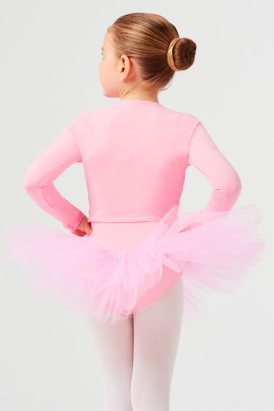 Ein junges Mädchen in einem rosa Ballett-Outfit und Tutu steht mit den Händen in den Hüften und blickt von der Kamera weg.