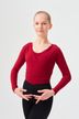 Junge Person in rotem Langarmshirt und schwarzer Hose posiert mit den Händen in Ballettposition vor schlichtem Hintergrund. 1