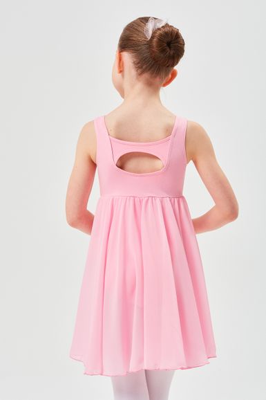 Ein junges Mädchen in einem rosa Ballettkleid steht mit hinter dem Rücken verschränkten Händen da und blickt von der Kamera weg.