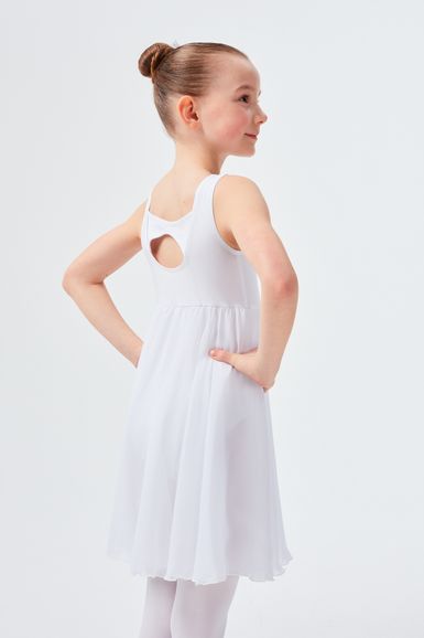 Ein junges Mädchen in einem weißen ärmellosen Kleid steht mit den Händen in den Hüften und blickt zur Seite.