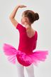 Ein junges Mädchen in einem rosa Ballett Trikot und Tutu steht mit erhobenem Arm da und blickt von der Kamera weg. 2
