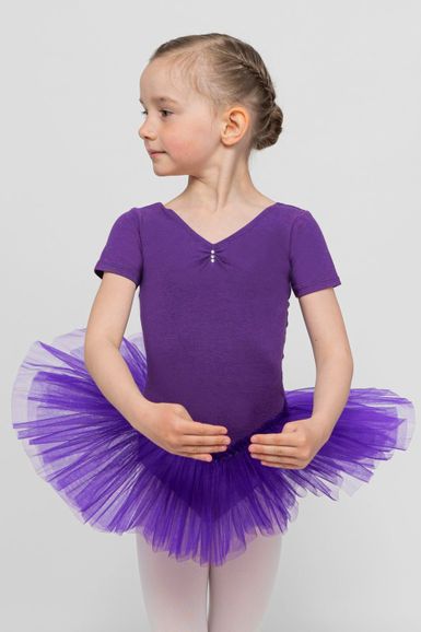 Junges Mädchen in einem lila Ballett Trikot und Tutu posiert in einer Ballettposition vor einem schlichten grauen Hintergrund.
