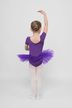 Ein kleines Kind in einem lila Ballett-Outfit und weißen Strumpfhosen posiert mit einem erhobenen Arm und blickt von der Kamera weg. 2