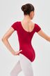 Eine Balletttänzerin in einem roten Ballett Trikot und weißen Strumpfhosen posiert mit ausgestrecktem Arm 2