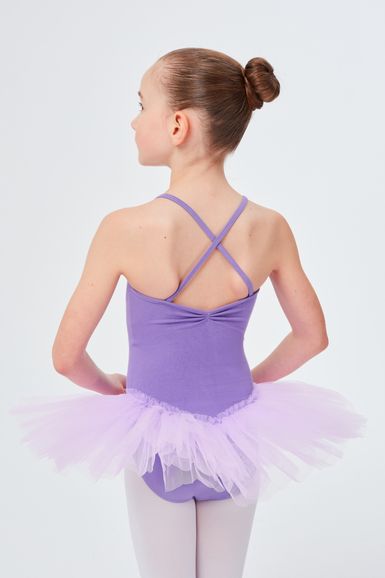 Ein junges Mädchen in einem lavendelfarbenen Ballett Trikot und Tutu steht mit den Händen in den Hüften und blickt von der Kamera weg.