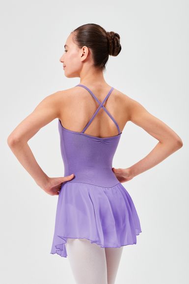 Eine Balletttänzerin in einem lila Ballett Trikot und Rock steht mit den Händen in den Hüften und blickt von der Kamera weg.