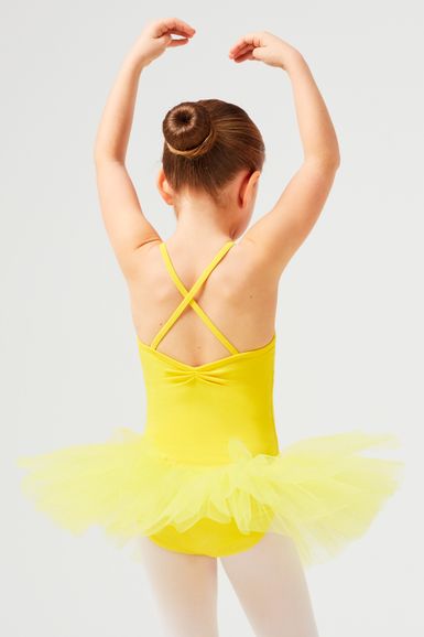 Ein junges Mädchen in einem gelben Tutu und Ballettschuhen posiert mit erhobenen Armen