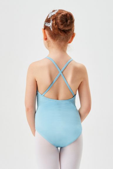 Ein junges Mädchen in einem blauen Ballettbody und weißen Strumpfhosen steht mit dem Rücken zur Wand