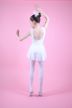 Eine junge Balletttänzerin in einem weißen Outfit posiert mit erhobenen Armen vor einem schlichten rosa Hintergrund. 6