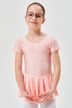 Ein junges Mädchen in rosa Ballett-Outfit steht mit vor der Brust verschränkten Händen vor der Kamera. 1