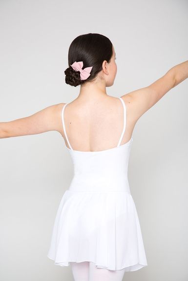 Eine Balletttänzerin in einem weißen Kostüm mit einer rosa Schleife im Haar steht mit ausgestreckten Armen da und blickt abgewandt.