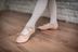Eine Person in weißen Strumpfhosen und rosa Ballettschuhen steht in Tanzposition auf einem Holzboden. 8