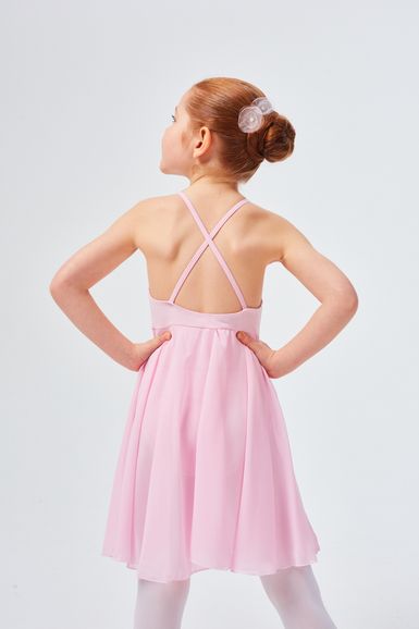 Mädchen in einem rosa Kleid mit gekreuzten Trägern steht mit den Händen in den Hüften und blickt von der Kamera weg.