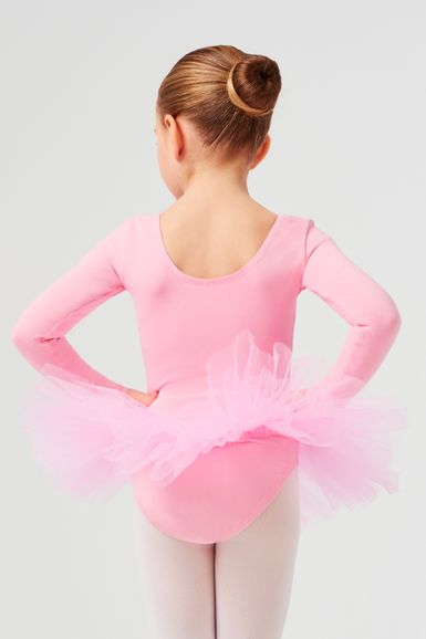 Ein junges Mädchen in einem rosa Ballettbody und Tutu steht mit den Händen in den Hüften und blickt von der Kamera weg.