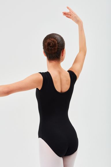 Eine Person in einem schwarzen Ballett Trikot und weißen Strumpfhosen posiert mit erhobenen Armen