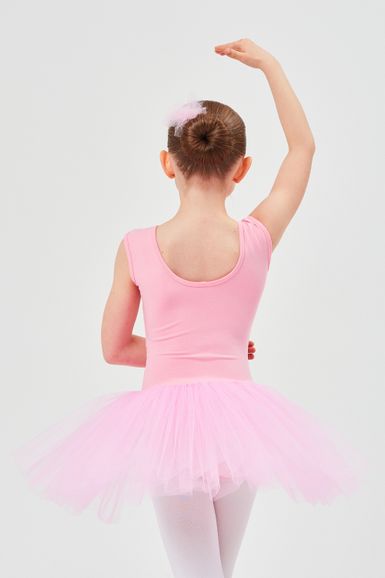 Ein junges Mädchen in einem rosa Ballett-Outfit posiert mit erhobenem Arm und dem Rücken zur Kamera.