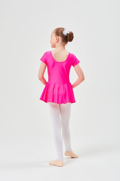 Ein junges Mädchen in einem rosa Ballett Trikot und weißen Strumpfhosen steht in Ballettposition und blickt von der Kamera weg.