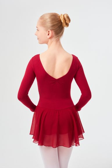 Eine junge Ballerina in einem roten Ballett Trikot und Rock steht mit dem Rücken zur Kamera.