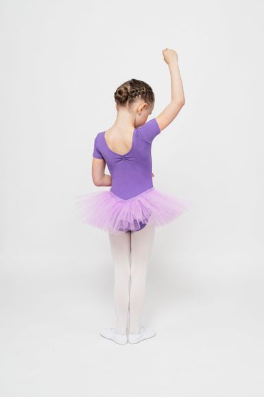 Ein junges Mädchen in einem lila Ballett Trikot und Tutu steht mit abgewandtem Blick da