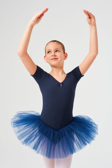 Junges Mädchen in einem marineblauen Ballett Trikot und Tutu posiert mit erhobenen Armen in einer Ballettposition.