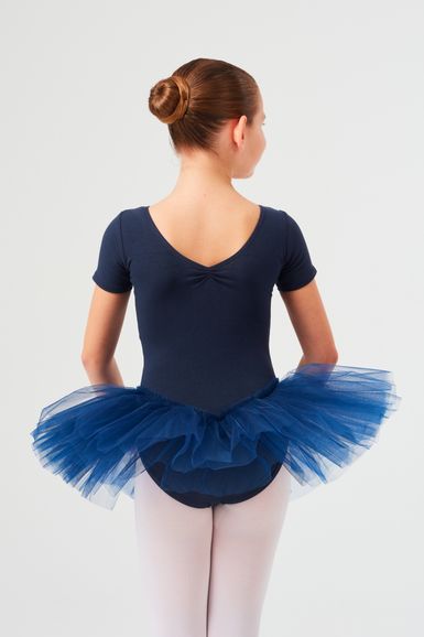 Ein junges Mädchen in einem marineblauen Ballett Trikot und Tutu steht mit dem Rücken zur Wand