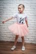 Junges Mädchen in einem rosa Tutu und einem weißen T-Shirt posiert in einer Tanzhaltung vor einer weißen Backsteinwand. 1