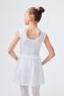 Ein junges Mädchen in einem weißen Ballett-Outfit steht mit den Händen in den Hüften und blickt von der Kamera weg. 2