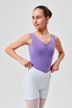 Eine junge Balletttänzerin in einem lila Ballett Trikot und weißen Shorts steht mit den Händen in den Hüften da und schaut zur Seite. 1
