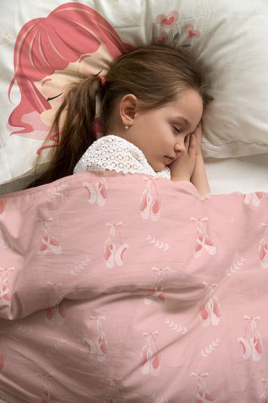Ein junges Mädchen schläft auf einem Bett mit einer rosa Decke mit Ballettschuhen und einem Kissen mit dem Gesicht eines Cartoon-Mädchens.