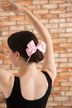 Ein Mädchen in einem schwarzen Ballettanzug mit einer rosa Schleife im Haar posiert vor einer Backsteinmauer.