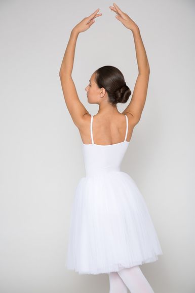 Eine Ballerina in einem weißen Tutu steht mit erhobenen Armen auf Spitze und blickt von der Kamera weg.
