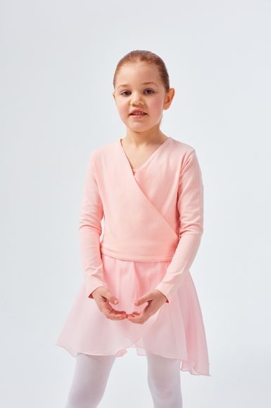 Junges Mädchen in einem rosa Ballett-Outfit steht mit leicht gefalteten Händen und blickt in die Kamera.