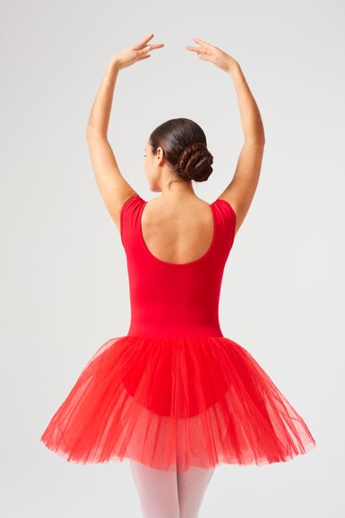 Eine Balletttänzerin in einem roten Tutu steht mit erhobenen Armen in der ersten Position