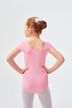 Ein junges Mädchen in einem rosa Ballettbody und weißen Strumpfhosen steht mit den Händen in den Hüften und blickt von der Kamera weg. 2