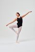 Eine Balletttänzerin in einem schwarzen Trikot und weißen Strumpfhosen posiert in einem Studio auf einem Bein mit ausgestreckten Armen.