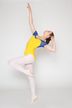 Eine Balletttänzerin in einem gelb-blauen Trikot posiert auf einem Bein mit ausgestreckten Armen.