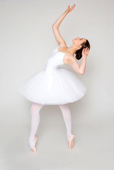 Eine Ballerina in einem weißen Tutu steht mit erhobenen Armen auf Spitze und posiert.
