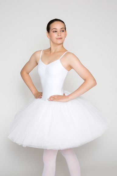 Eine Balletttänzerin in einem weißen Tutu und Trikot steht mit den Händen in den Hüften.