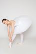 Eine Balletttänzerin in einem weißen Tutu und Spitzenschuhen beugt sich nach vorne und berührt ihren Knöchel.