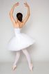 Balletttänzerin in weißem Tutu und Spitzenschuhen steht auf Spitze mit erhobenen Armen und blickt von der Kamera weg.