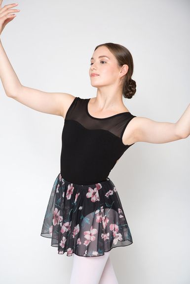 Eine Balletttänzerin posiert mit erhobenen Armen und trägt einen schwarzen Trikotanzug und einen geblümten Rock.
