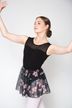 Eine Balletttänzerin posiert mit erhobenen Armen und trägt einen schwarzen Trikotanzug und einen geblümten Rock.