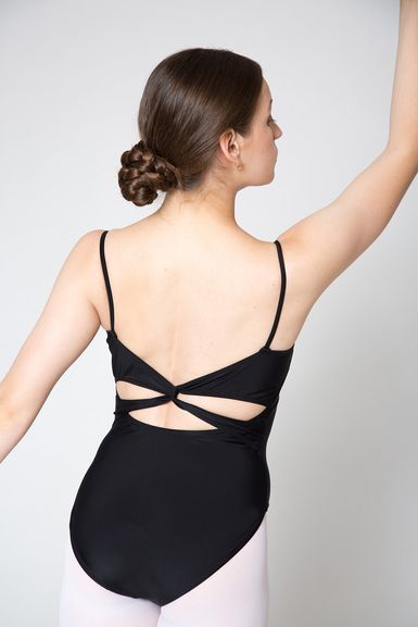 Eine Frau in einem schwarzen Trikot mit gekreuzten Rückenträgern und einem ordentlichen Dutt posiert mit einem erhobenen Arm und dem Gesicht nach außen.