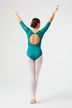 Eine Balletttänzerin in einem blaugrünen Trikot und weißen Strumpfhosen steht mit erhobenen Armen und dem Rücken zur Kamera.