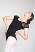 Eine Balletttänzerin in einem schwarzen Trikot und weißen Strumpfhosen posiert mit den Händen in den Hüften und wölbt ihren Rücken.