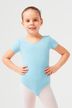 Junges Mädchen in einem hellblauen Ballettbody und weißen Strumpfhosen posiert mit den Händen in den Hüften. 1
