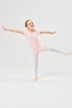 Ein junges Mädchen in einem rosa Trikot und weißen Strumpfhosen balanciert mit ausgestreckten Armen auf einem Bein und posiert in einem Tanzstudio. 3