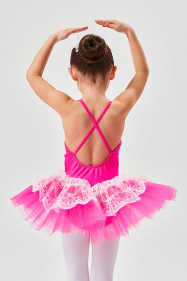 Ein junges Mädchen in einem rosa Tutu und weißen Strumpfhosen posiert mit über dem Kopf erhobenen Armen und blickt von der Kamera weg.