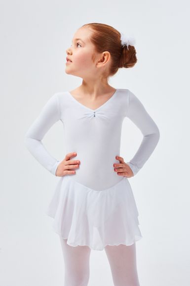 Ein junges Mädchen in einem weißen Ballett-Outfit steht mit den Händen in den Hüften und blickt zur Seite.